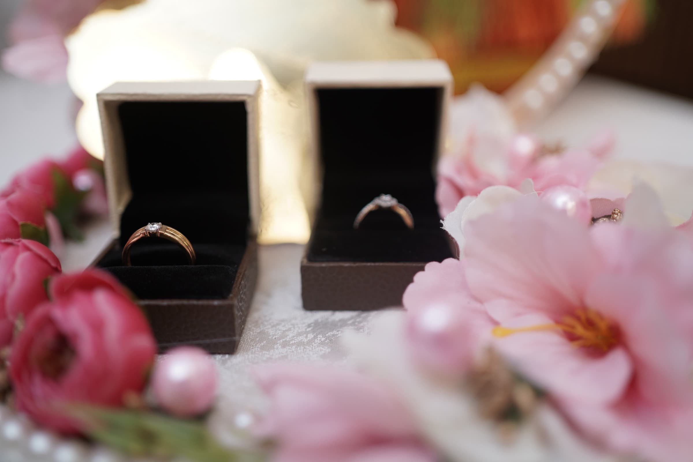 Two ring boxes surrounded by blush flowers, with Mayank's ring in focus